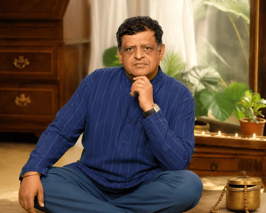 Acharya Gautam P Nayak seated cross-legged in his consultation room in Mumbai, with lit diyas and a brass kalash beside him